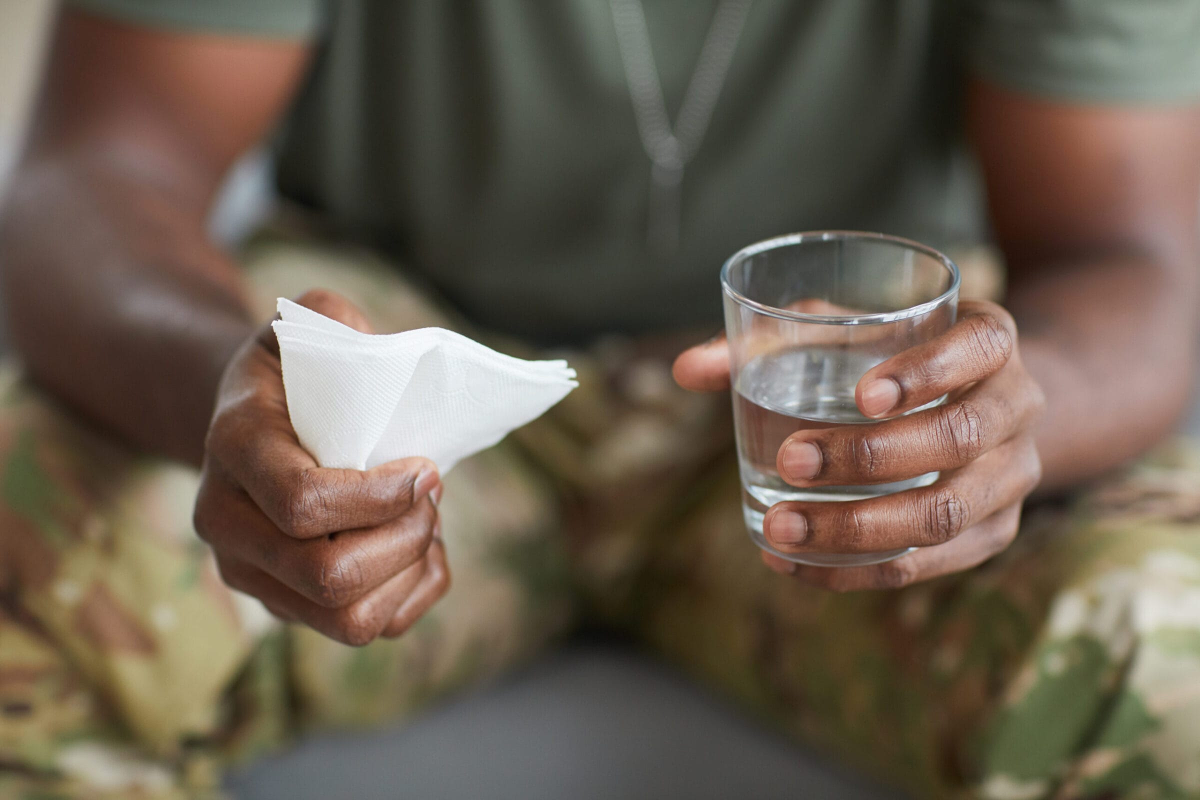 Close-up of man in uniform sitting with glass of water and napkin in his hands