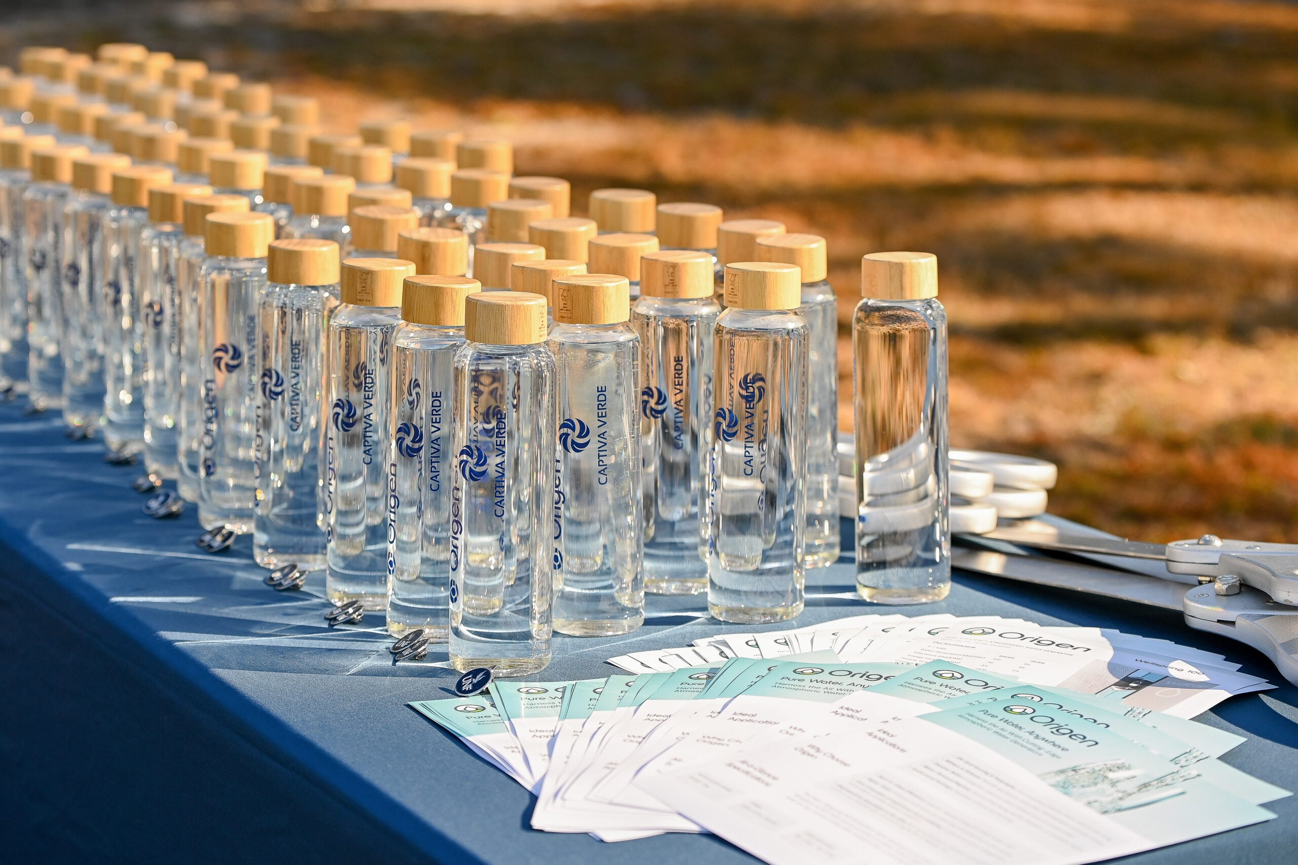 Clear glass water bottles with wooden caps arranged on a table, alongside printed materials and scissors.
