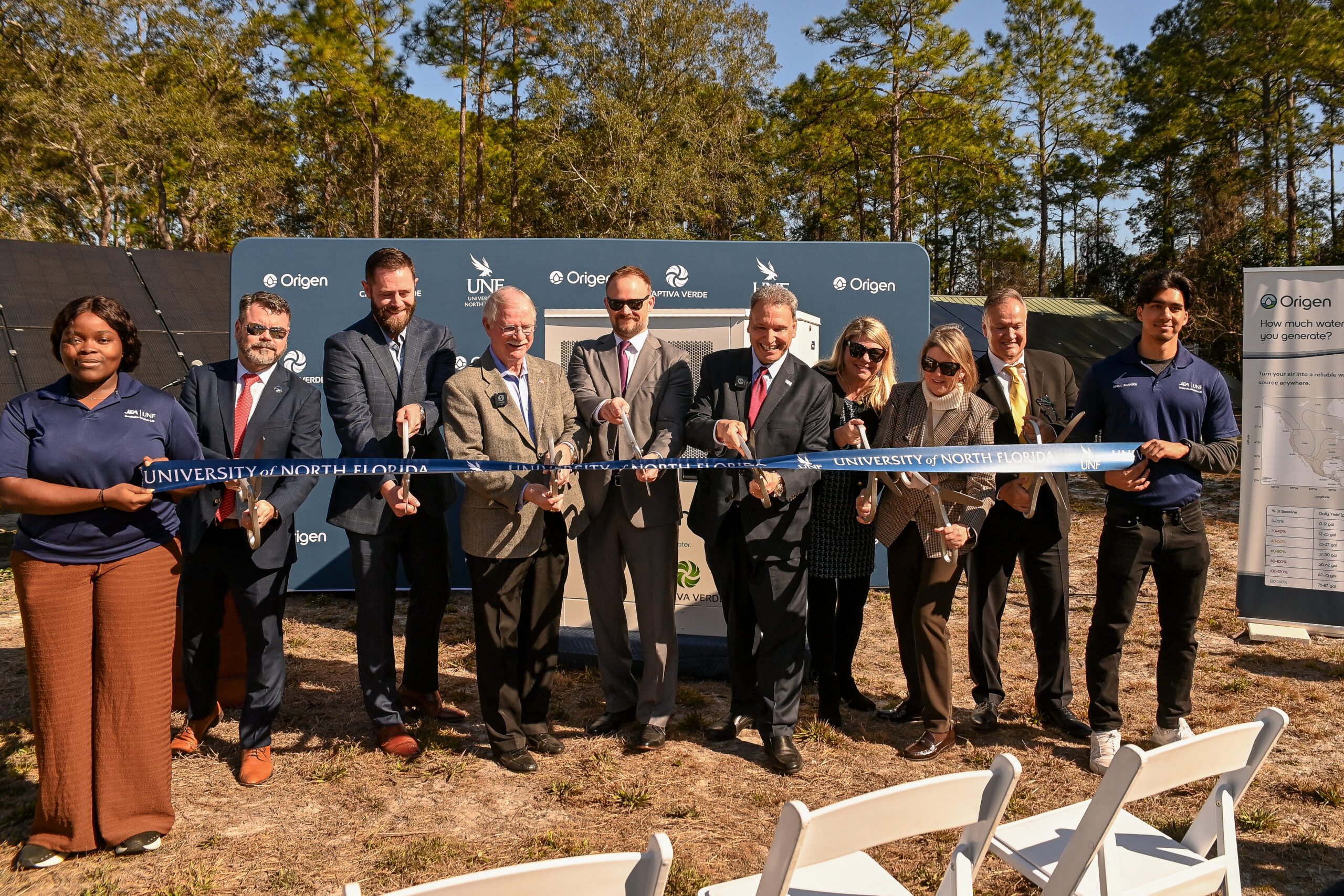 Officials cut a ribbon at the University of North Florida, celebrating a new solar project with solar panels in the background.