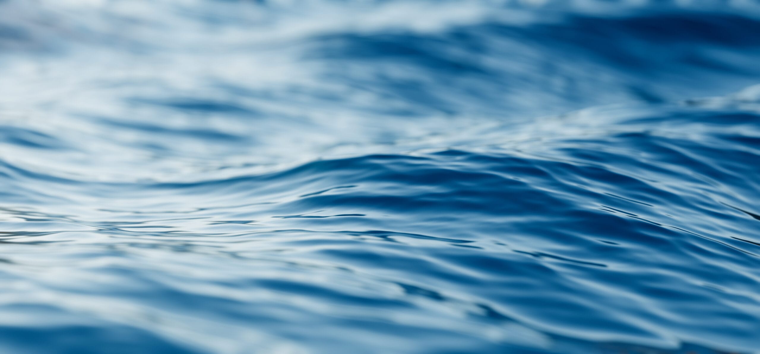 Gentle ripples on a serene blue water surface, reflecting light and creating a calming, fluid texture.