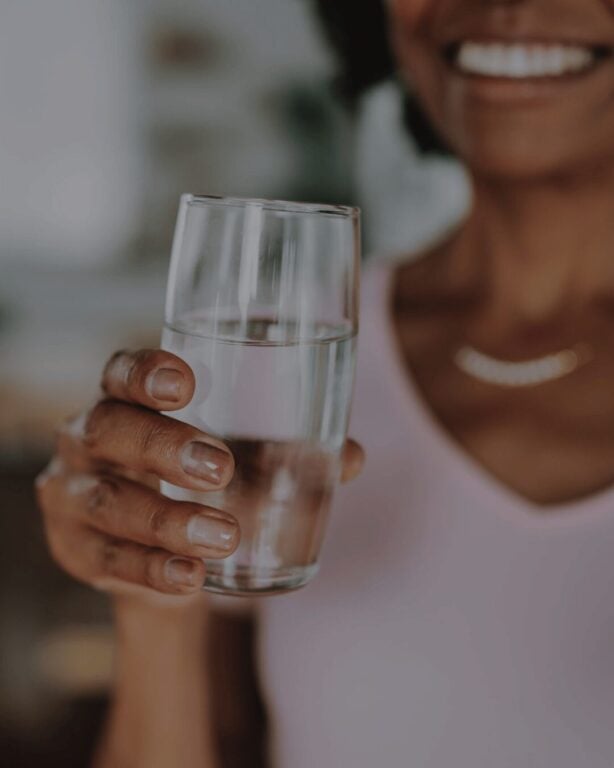 Woman holding a glass of water, smiling.