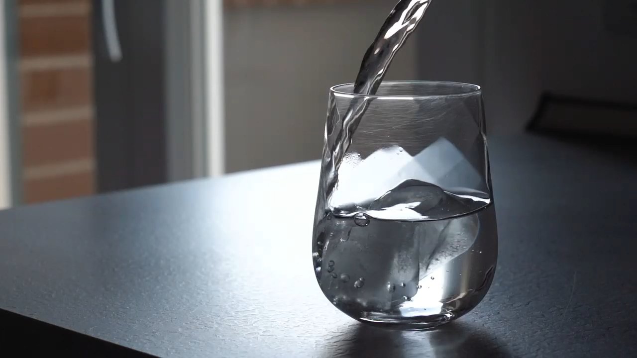 Water pouring into a clear glass on a dark surface.