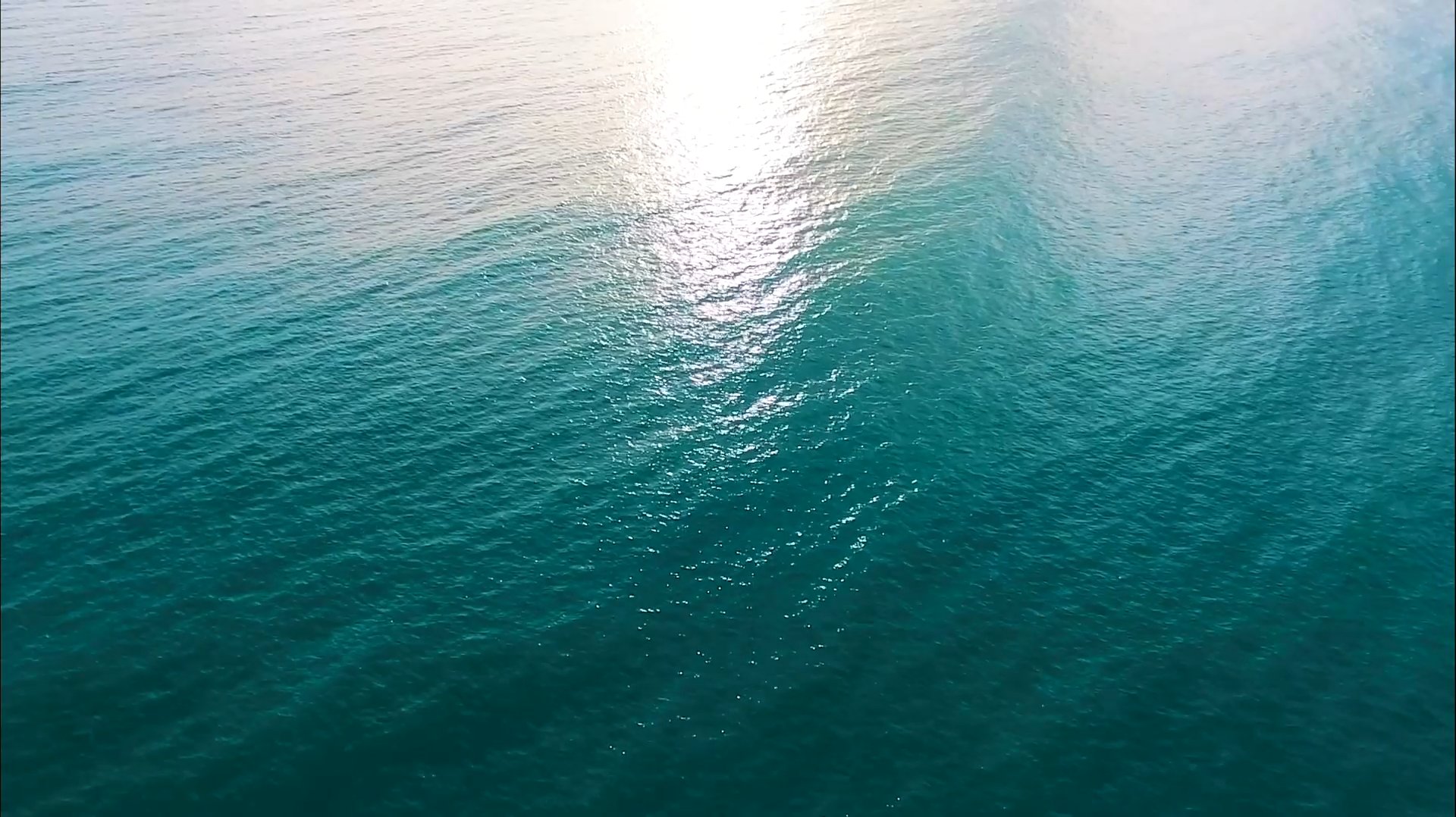 Sunlight glinting on rippling teal ocean water.