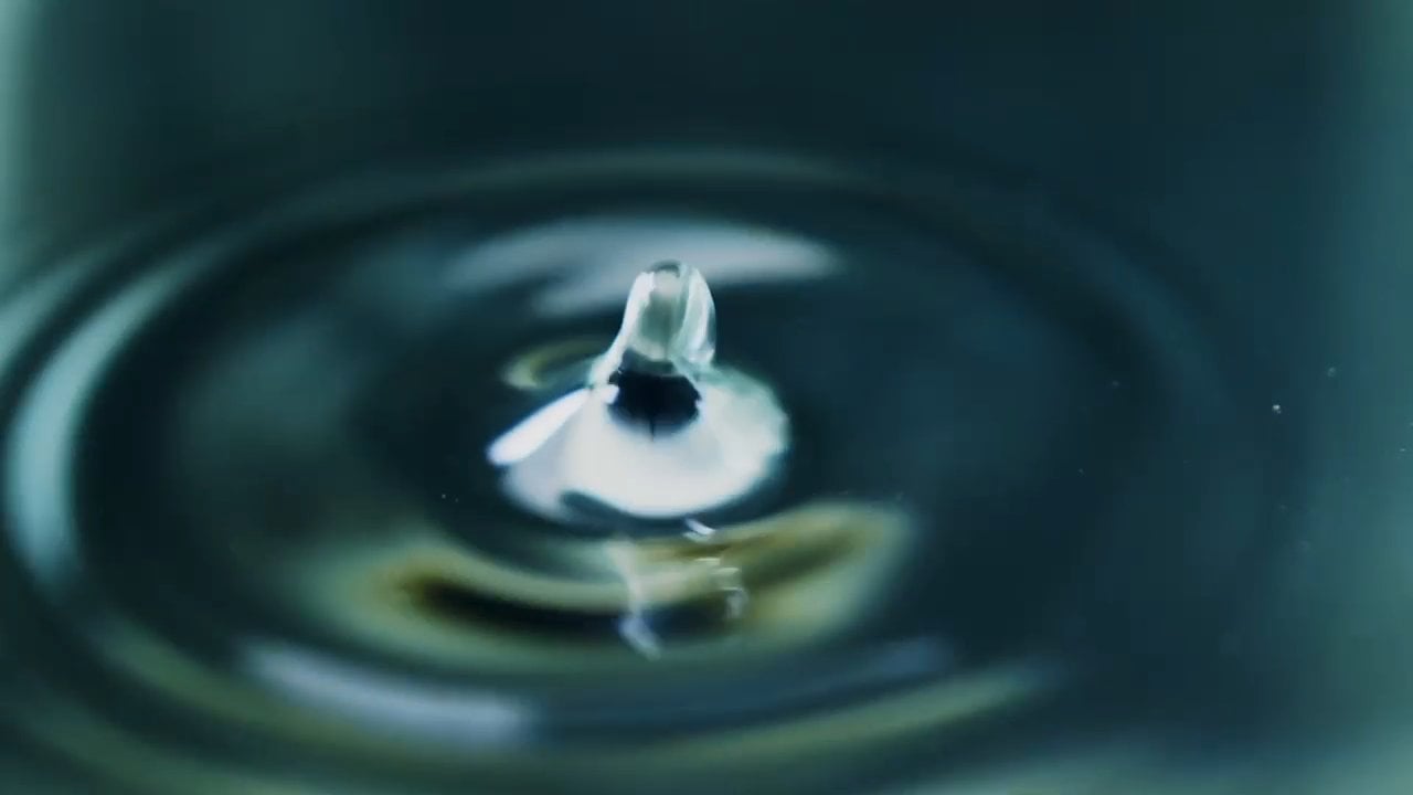 Water drop impacting surface, creating ripples.