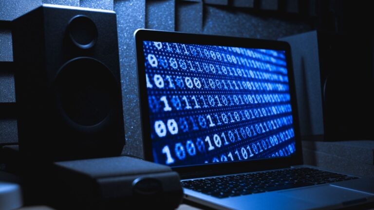 Laptop displaying binary code next to a speaker.